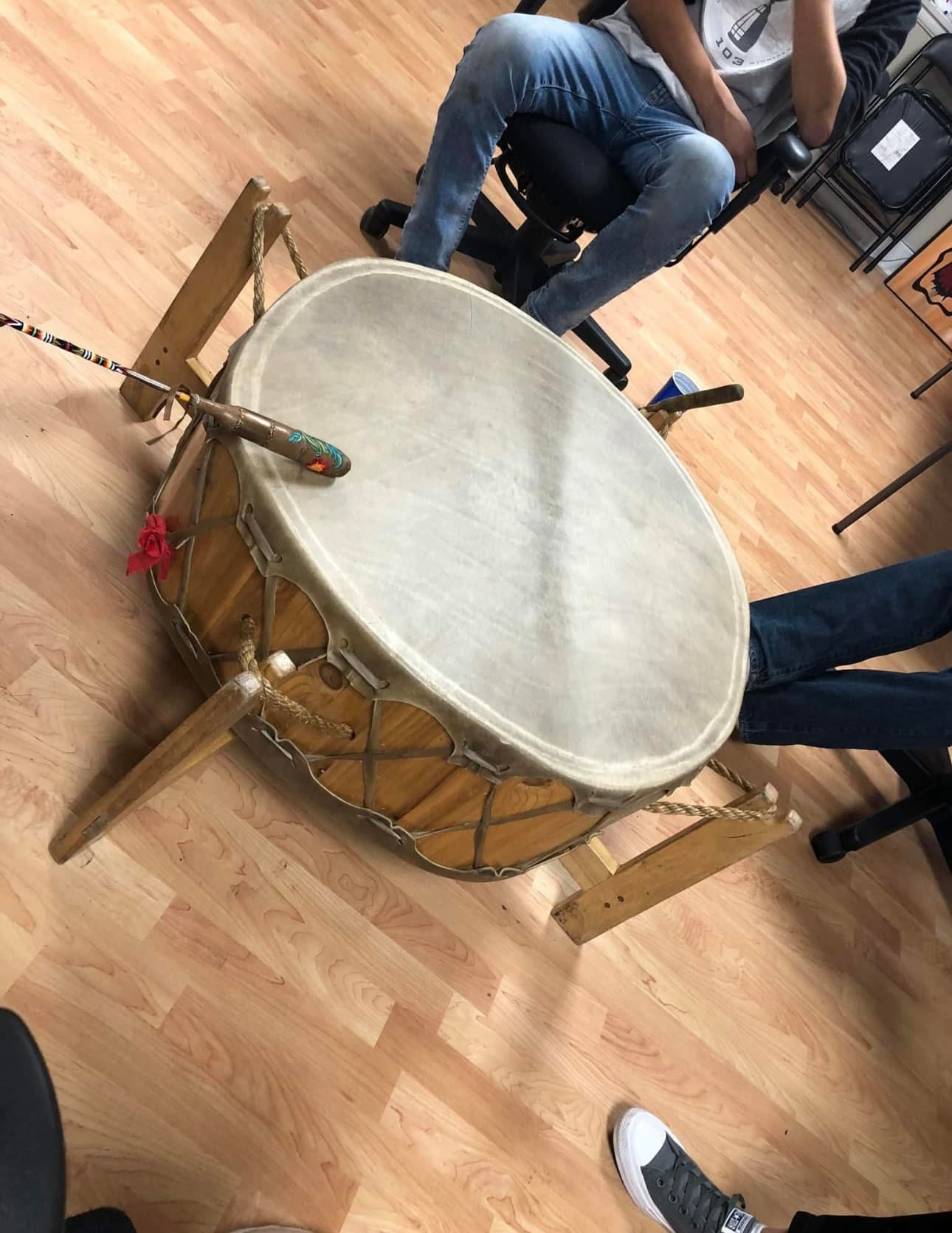 A large drum resting on a wooden stand with people seated around it