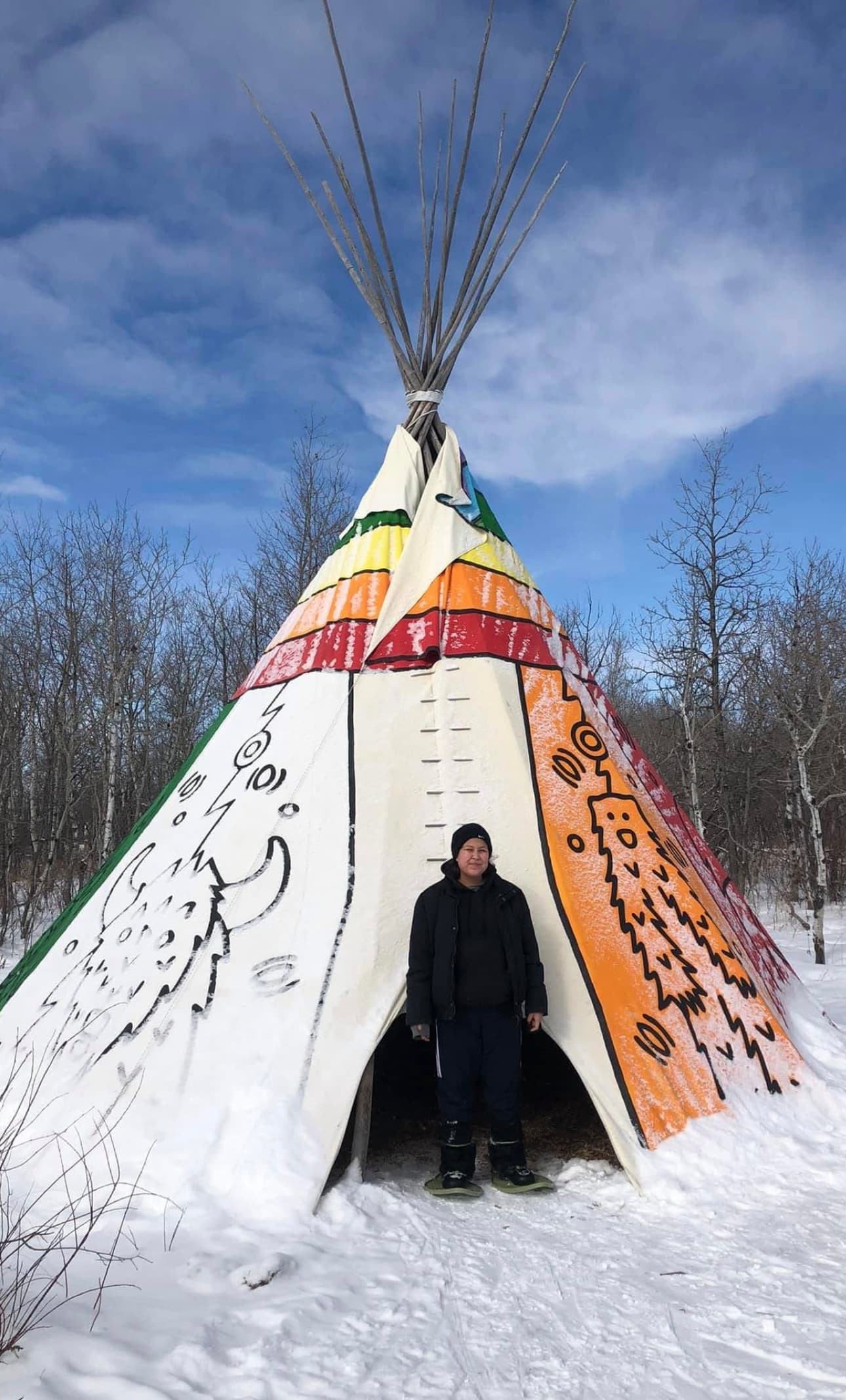 A young person standing at the entrance of a painted tipi on a snowy winter day