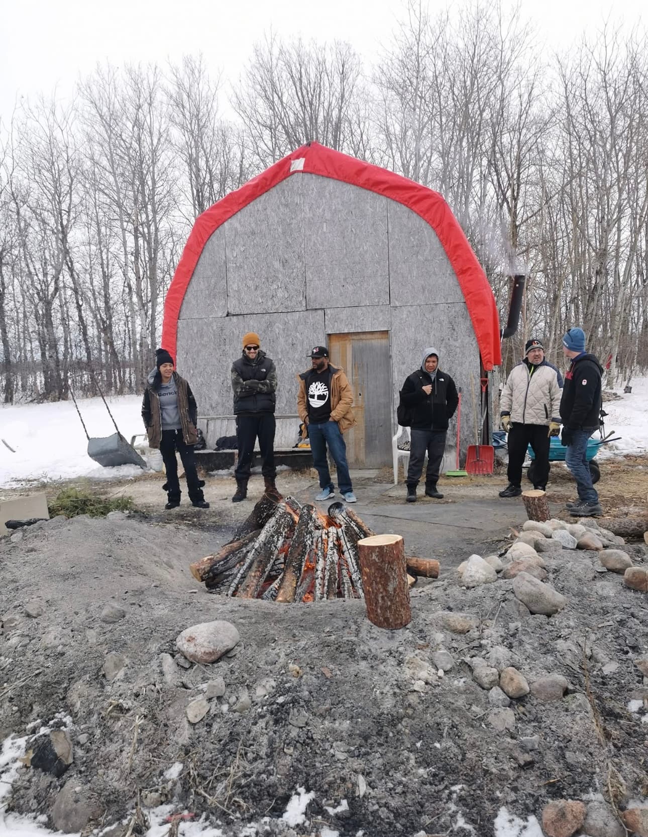 Group gathered around a fire near a sweat lodge in winter