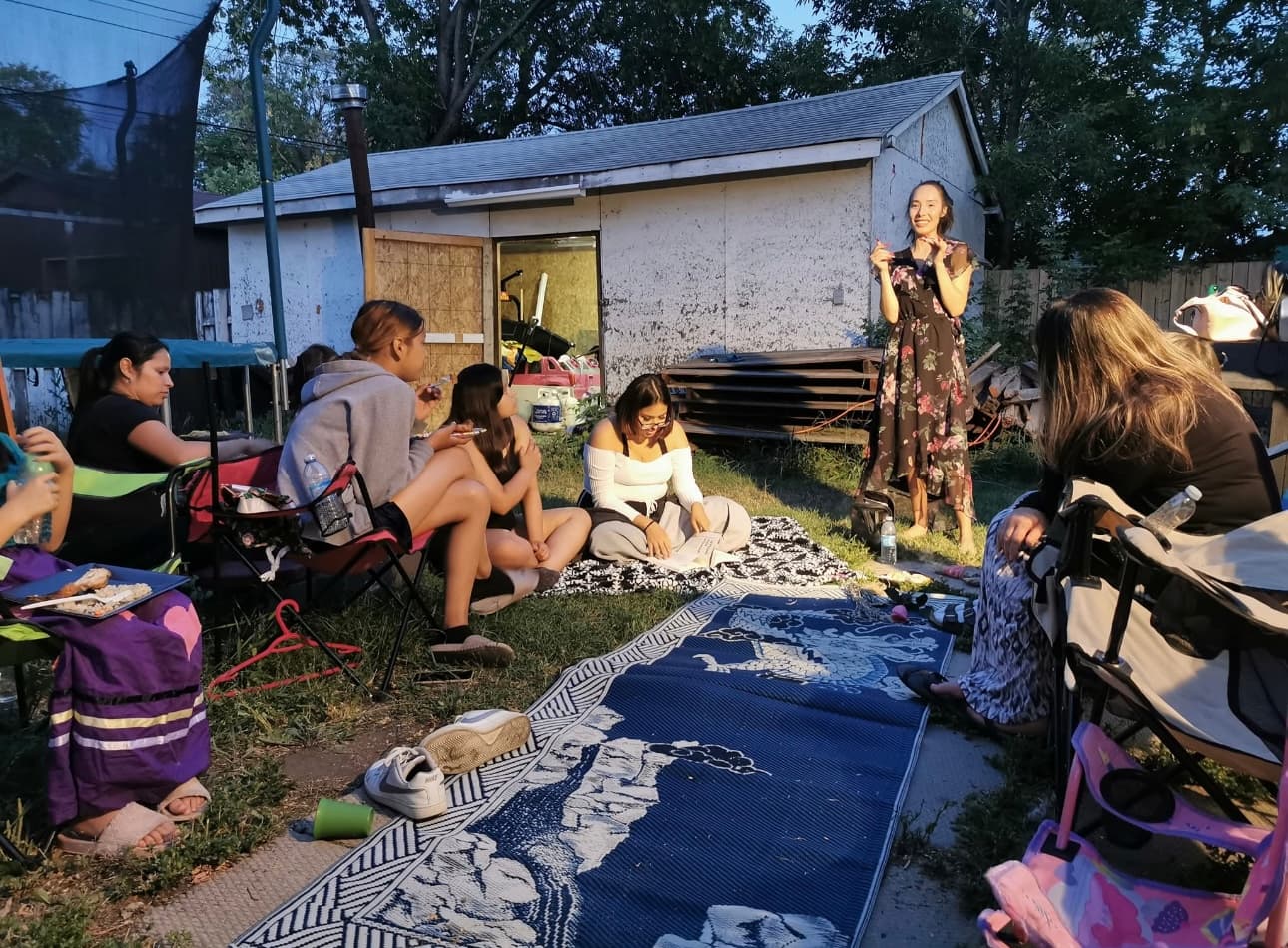 Youth and adults sitting together on blankets and camp chairs at an outdoor evening gathering